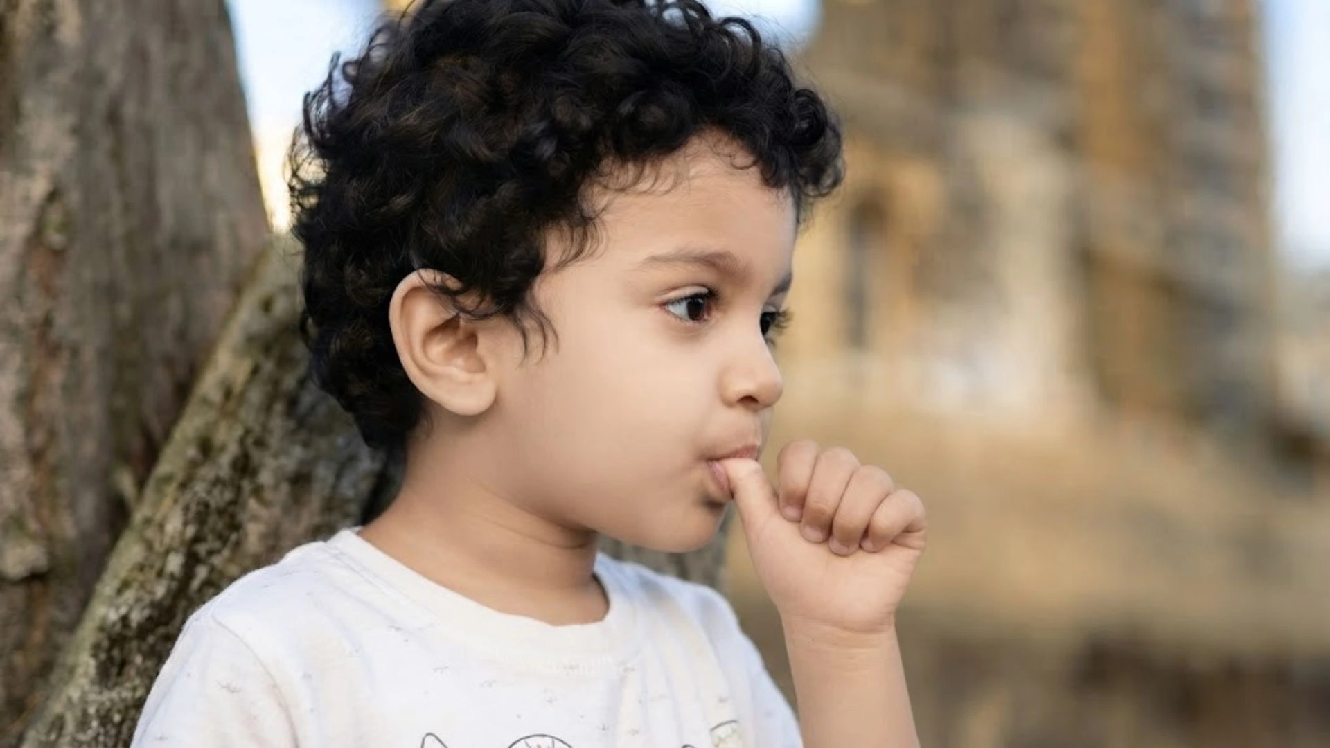 Young boy sucking his thumb while standing outdoors.
