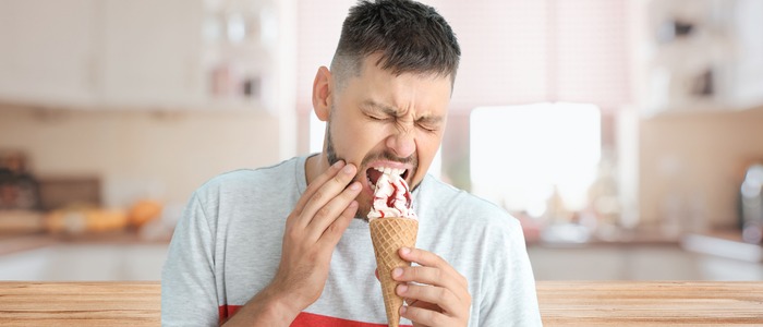 Person experiencing tooth sensitivity and discomfort while eating ice cream due to cavities, tooth decay, and weakened enamel.